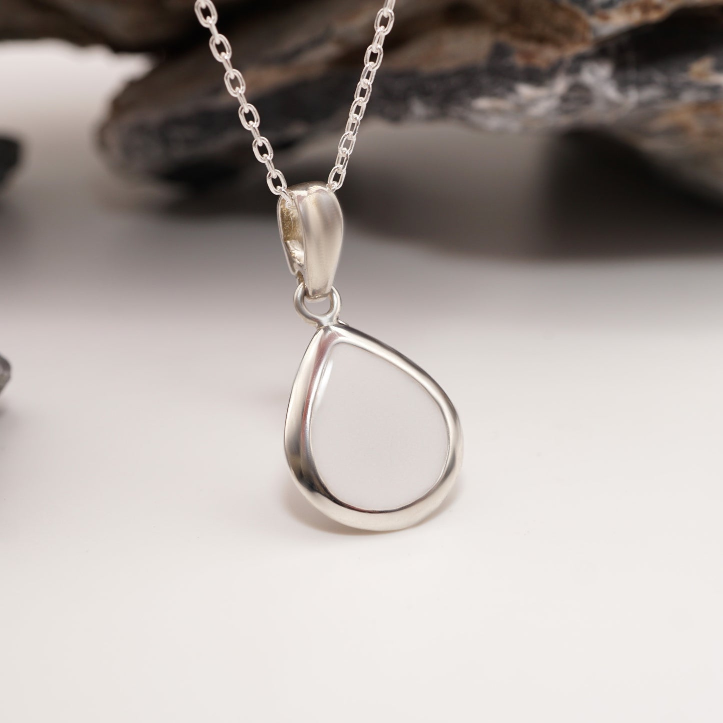 Teardrop-shaped sterling silver pendant with a daring semen inlay, displayed against natural stones for bold, modern jewellery.