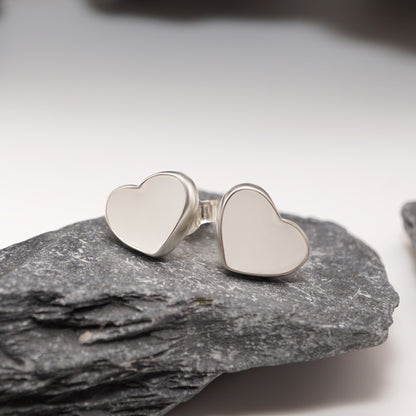 Heart-shaped sterling silver earrings with semen inlays, elegantly displayed against a natural stone backdrop for bold intimate jewellery.